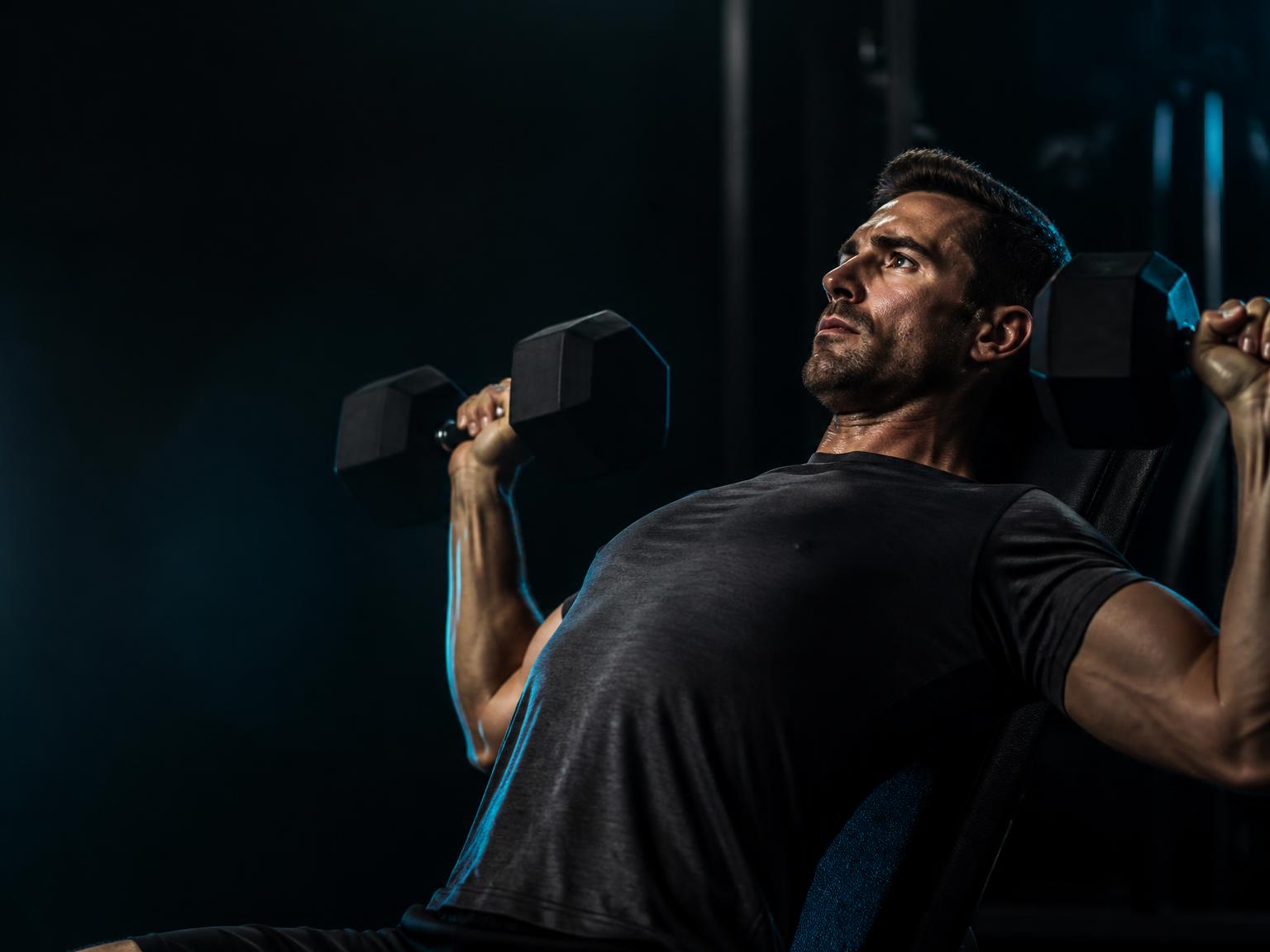 Athlete performing an incline dumbbell press in a dark studio gym